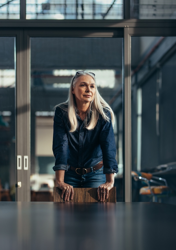 Woman leaning on a chair next to a table, looking off into the distance